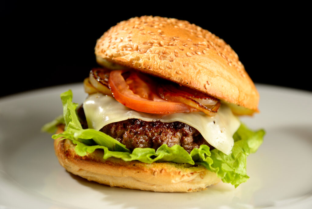 Hamburger with onion, bacon and salad on black background